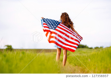 Young woman with american USA flag on blooming meadow. Independence Day, 4th July. Young woman with american USA flag on blooming meadow. Independence Day, 4th July. 127356937