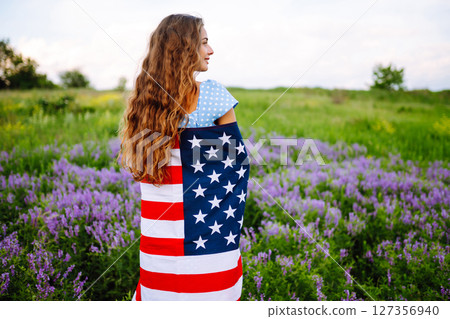 Young woman with american USA flag on blooming meadow. Independence Day, 4th July. Young woman with american USA flag on blooming meadow. Independence Day, 4th July. 127356940