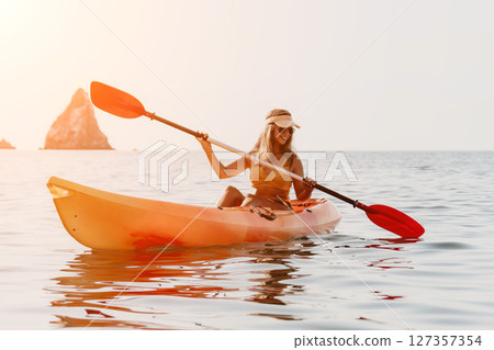Woman Kayaking Ocean Paddle Sport - Young woman paddling a kayak in the ocean with a scenic background. 127357354