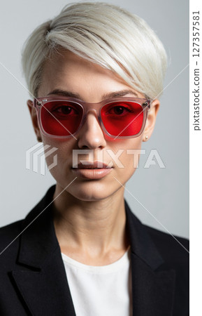 White woman with short pixie cut and red-tinted rectangular glasses, her confident eyes framed by sharp angular patterns, representing transformation 127357581