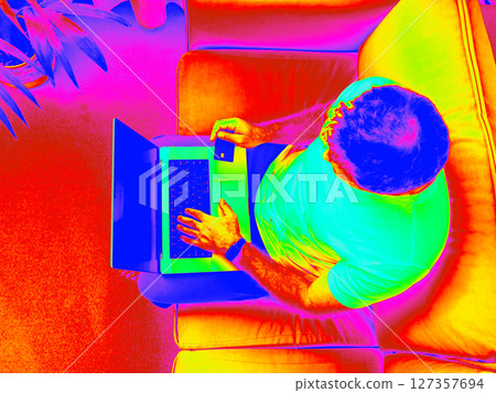 Infrared Thermal Image of man using laptop in living room interior. Overhead shot of man entering bank card information on laptop in modern minimalist living room Infrared Thermal Image of man using laptop in living room interior. Overhead shot of man entering bank card information on laptop in modern minimalist living room 127357694