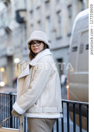 Fashionable individual in cozy winter attire enjoys a stroll through a bustling city street on a calm afternoon, embodying style and comfort seamlessly 127358609