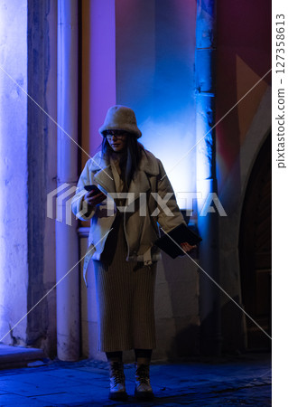 A captivating evening stroll taken by a fashion enthusiast through a bustling urban landscape immersed in stunning blue lights all around 127358613