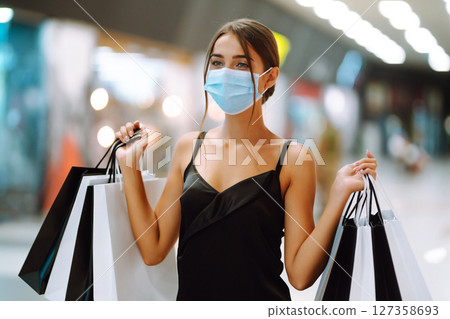 Fashionable woman in protective medical mask with shopping bags walking in the mall. Covid-19. 127358693
