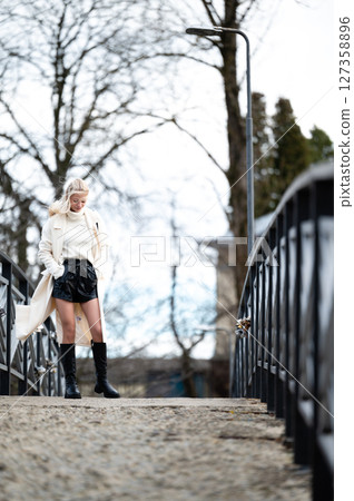 Fashionable woman in black and white attire walks on a charming bridge amidst a picturesque landscape during a cloudy day in early spring Fashionable woman in black and white attire walks on a charming bridge amidst a picturesque landscape during a cloudy day in early spring 127358896