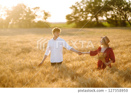 Young happy couple hugging on a wheat field, on the sunset. Enjoying time together. 127358950