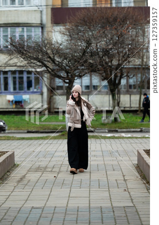 Chilly afternoon stroll through a quiet urban park with trees and distant figures on the path while dressed in cozy winter attire 127359157