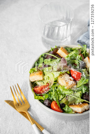 Salad with lettuce, tomatoes, croutons, olives and parmesan cheese in a bowl on a light background 127359256