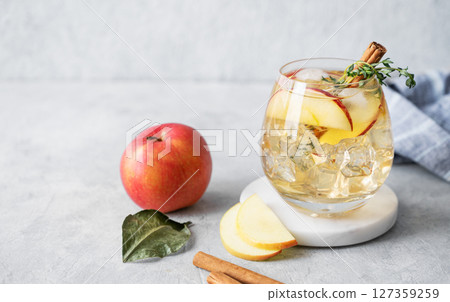 Apple cocktail or cider with ice, garnished with cinnamon and thyme in a glass on a marble stand Apple cocktail or cider with ice, garnished with cinnamon and thyme in a glass on a marble stand 127359259