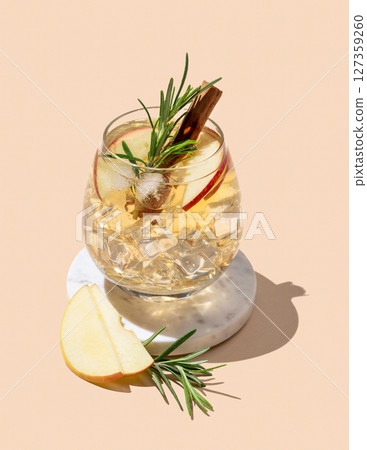 Apple cocktail or cider in a glass with ice, cinnamon and rosemary on a marble stand 127359260