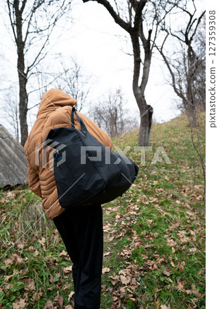 Hiker in a warm coat carrying a large bag while walking through a leaf-strewn trail on a cool autumn day in a serene wooded area Hiker in a warm coat carrying a large bag while walking through a leaf-strewn trail on a cool autumn day in a serene wooded area 127359308
