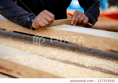 Male carpenter hand placing a piece of wood and use pencil to draw a line for cutting wooden plank Male carpenter hand placing a piece of wood and use pencil to draw a line for cutting wooden plank 127359592