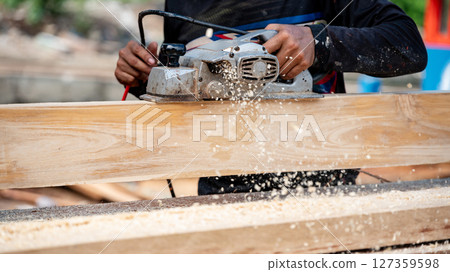 Male carpenter hand using an electric planer on wooden plank at construction site 127359598