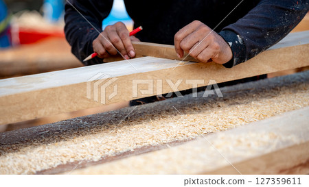 Male carpenter hand placing a piece of wood and use pencil to draw a line for cutting wooden plank 127359611