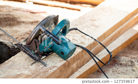 Electric circular saw on timber stack in a wood workshop Electric circular saw on timber stack in a wood workshop 127359617
