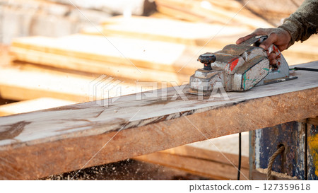 Male carpenter hand using an electric planer on wooden plank in workshop Male carpenter hand using an electric planer on wooden plank in workshop 127359618