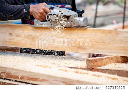 Male carpenter hand using an electric planer on wooden plank in workshop Male carpenter hand using an electric planer on wooden plank in workshop 127359625