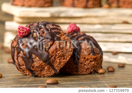 Round chocolate cakes. Decorated with candied raspberries. Wooden background. 127359970