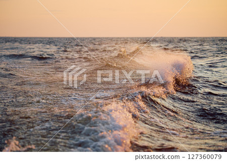 The wave splashes into splashes in the rays of sun at sunset 127360079