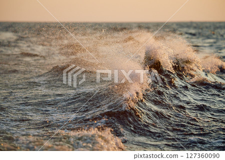 The wave splashes into splashes in the rays of sun at sunset 127360090
