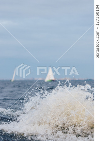 Sailing regatta in the Gulf of Finland at sunset, sailing yacht competing in a race, splashing water from under the boat, teamwork, board the boat Sailing regatta in the Gulf of Finland at sunset, sailing yacht competing in a race, splashing water from under the boat, teamwork, board the boat 127360104