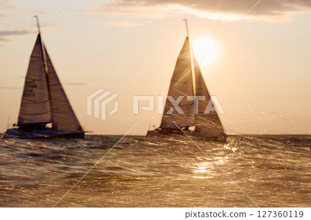 Sailing regatta in the Gulf of Finland at sunset, two sailing yachts competing in a race, splashing water from under the boats, teamwork, board the boat 127360119