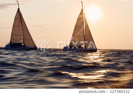 Two sailboats are moving at high speed at sunset, sailing regatta in the Gulf of Finland at sunset, sailing yacht competing in a race, splashing water from under the boat, teamwork, board the boat 127360132