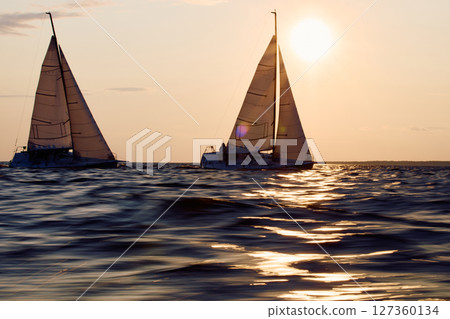 Two sailboats are moving at high speed at sunset, sailing regatta in the Gulf of Finland at sunset, sailing yacht competing in a race, splashing water from under the boat, teamwork, board the boat 127360134