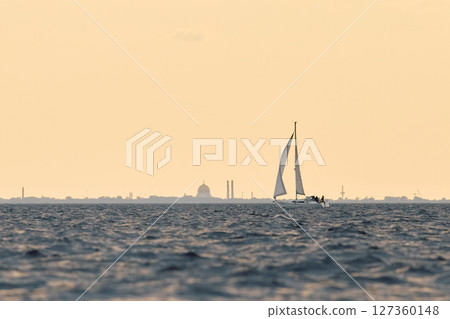 The lonely sailboat at sunset, the Naval Cathedral in Kronstadt on background, Sailing regatta in the Gulf of Finland at sunset, sailing yacht competing in a race, splashing water, board the boat 127360148
