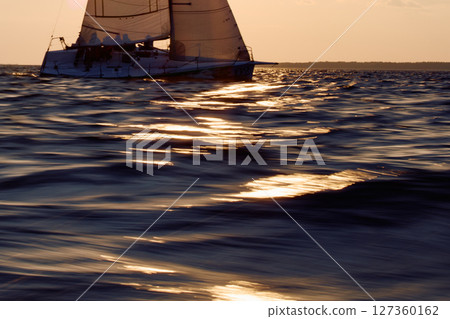 The sailboat is moving at high speed at sunset, sailing regatta in the Gulf of Finland at sunset, sailing yacht competing in a race, splashing water from under the boat, teamwork, board the boat The sailboat is moving at high speed at sunset, sailing regatta in the Gulf of Finland at sunset, sailing yacht competing in a race, splashing water from under the boat, teamwork, board the boat 127360162