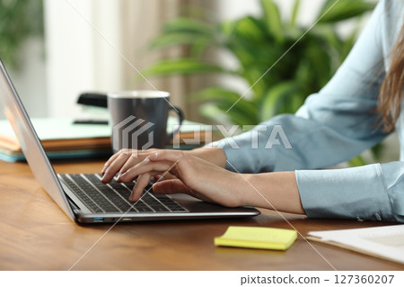 Woman hands working online typing on laptop on a wooden table 127360207
