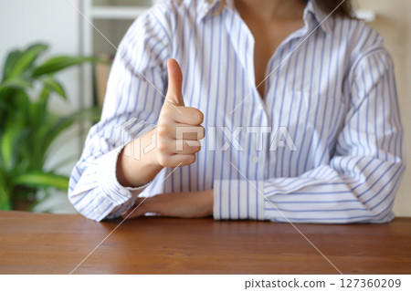 Woman gesturing thumbs up at home on a table Woman gesturing thumbs up at home on a table 127360209