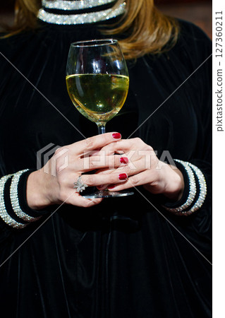 A glass of white wine or champagne in a woman's hand.  127360211