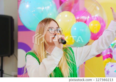 A funny young woman with a microphone is leading a children's party. A funny young woman with a microphone is leading a children's party. 127360213