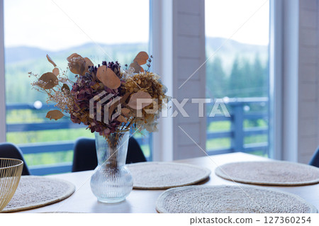 A Beautifully Decorated Dining Table Featuring a Vibrant Dried Flower Arrangement in a Cozy, Bright Setting with Stunning Nature Views in the Background 127360254