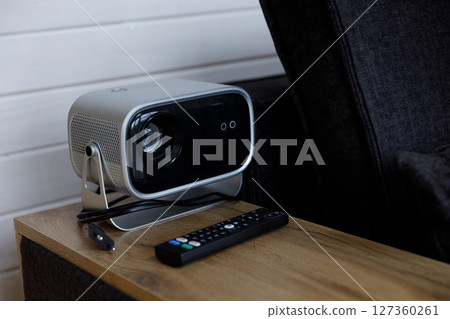 Modern Projector on a Wooden Table with Remote Control Nearby, Ideal for Home Theater Experience and Movie Nights in Cozy Living Room Decor 127360261
