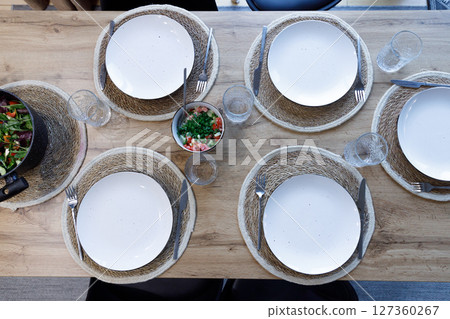 Inviting Dining Table Setting Featuring White Plates, Rustic Place Mats, and Fresh Ingredients for an Enjoyable Culinary Experience with Family and Friends 127360267