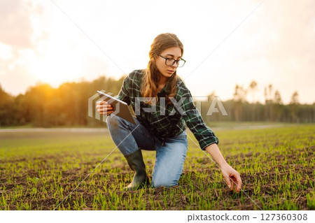 Farmer woman in boots checks the quality of the soil before sowing in her hands with digital tablet. 127360308
