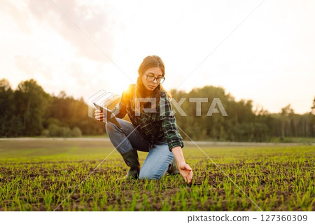 Farmer woman in boots checks the quality of the soil before sowing in her hands with digital tablet. 127360309