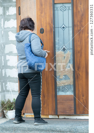 Woman waiting at a wooden door with a blue bag in a quiet neighborhood on a calm afternoon, eager for a friendly visit or an important delivery Woman waiting at a wooden door with a blue bag in a quiet neighborhood on a calm afternoon, eager for a friendly visit or an important delivery 127360331