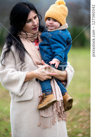 Gentle embrace a mother's love on a cool day while holding her child wearing yellow hat and denim jacket feeling safe and warm in her arms creating a cherished moment in time Gentle embrace a mother's love on a cool day while holding her child wearing yellow hat and denim jacket feeling safe and warm in her arms creating a cherished moment in time 127360342