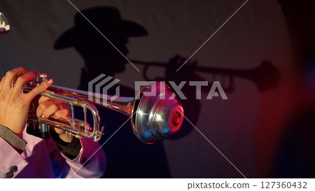 A man wearing a ten-gallon hat and playing a trumpet and his silhouette 127360432