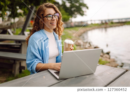 Beautiful female freelancer working online using laptop enjoying natural landscape overlooking lake. 127360452