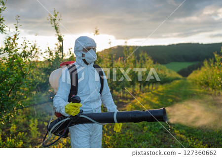Farmer spraying pesticide in orchard, disinfecting trees in protective suit. Farmer spraying pesticide in orchard, disinfecting trees in protective suit. 127360662