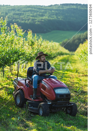 Farmer sitting on small tractor in orchard, enjoying peaceful moment. Farmer sitting on small tractor in orchard, enjoying peaceful moment. 127360694