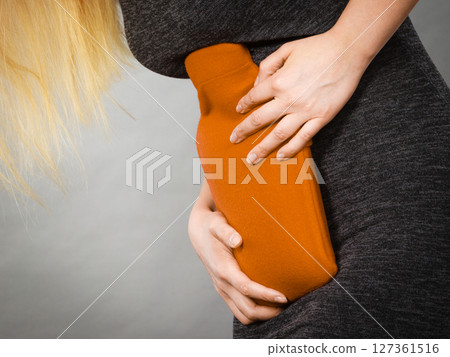 Girl having stomach ache, holding hot water bottle 127361516