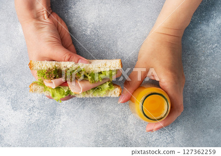 Delicious healthy sandwich for a snack breakfast in women hands. Toast bread tomato ham leaf salad, juice in a bottle, Delicious healthy sandwich for a snack breakfast in women hands. Toast bread tomato ham leaf salad, juice in a bottle, 127362259