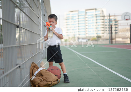 Young Boy Enjoying Water Break on Basketball Court Young Boy Enjoying Water Break on Basketball Court 127362386