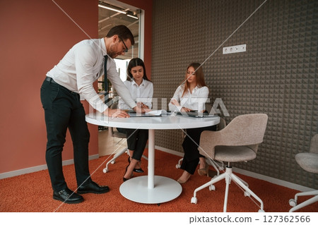 Man is talking, showing documents, plan of the project. Three business people are working in the office together Man is talking, showing documents, plan of the project. Three business people are working in the office together 127362566