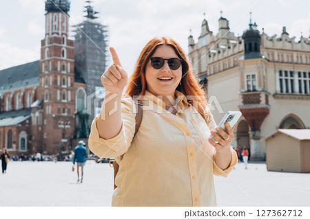 Beautiful stylish woman in sunglasses walking on Market Square in Krakow on summer day and holding mobile phone. Phone Communication. Urban lifestyle concept. Check social networks, send sms. 127362712